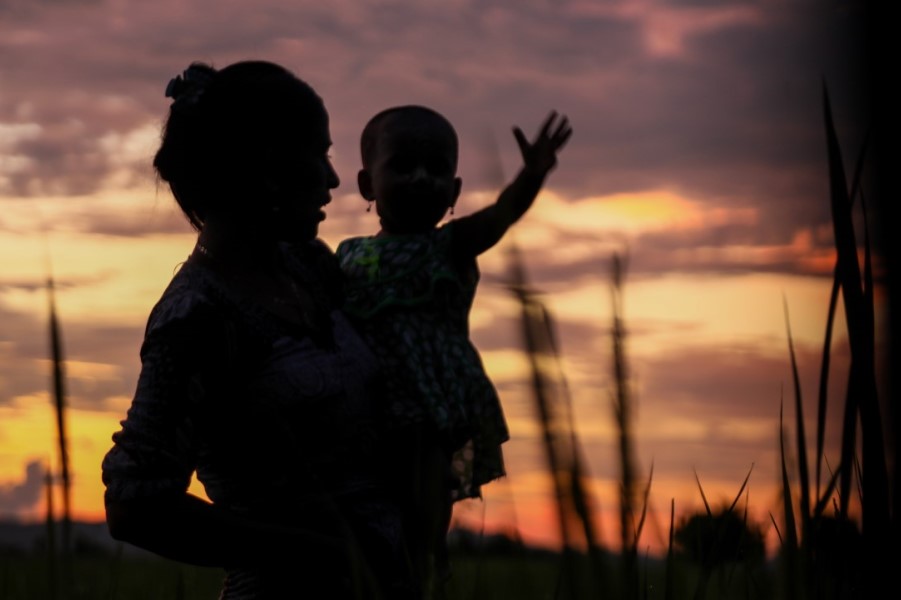 Silhouette of woman holding baby at sunset
